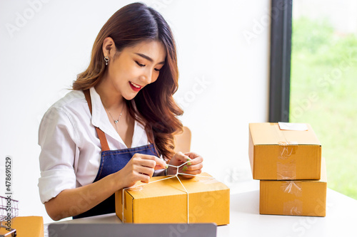 Small business owners look at company's past online sales, cropped image of woman tying up her own shipping box for delivery at online sales office, merchandising concept and modern businessman.