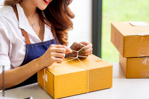 Small business owners look at company's past online sales, cropped image of woman tying up her own shipping box for delivery at online sales office, merchandising concept and modern businessman.
