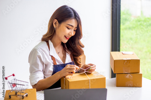 Small business owners look at company's past online sales, cropped image of woman tying up her own shipping box for delivery at online sales office, merchandising concept and modern businessman.