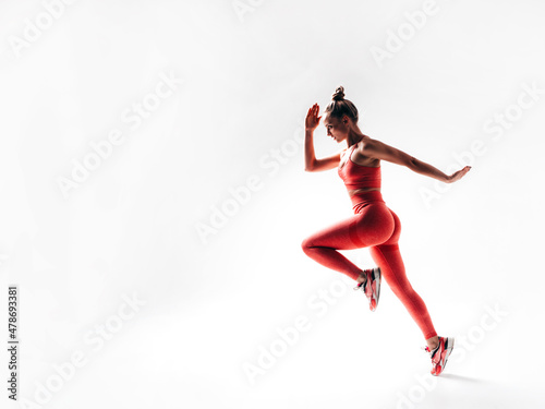 Fitness confident woman in pink sports clothing. Sexy young beautiful model with perfect body. Female isolated on white in studio. Cheerful and happy. Jumping and running