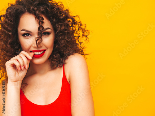 Closeup portrait of young beautiful smiling blond hipster female in trendy summer clothes. Sexy carefree woman posing in studio with afro curls hairstyle. Positive model having fun, isolated on yellow