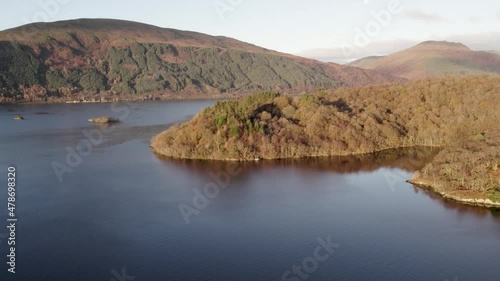 Left roll with righ pan aerial drone footage revealing Ben Lomond, Beinn Dubh and Beinn Bhreac mountains (Mounro) during an autumn sunrise with native broadleaf woodland and Loch Lomond foreground. photo