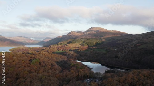 Left pan aerial drone shot of Loch Lomond and teh Trossachs National Park capturing Ben Lomond and Beinn Bhreac mountains and Dugn Lochan over autumnal native and non-native forests at sunrise. photo