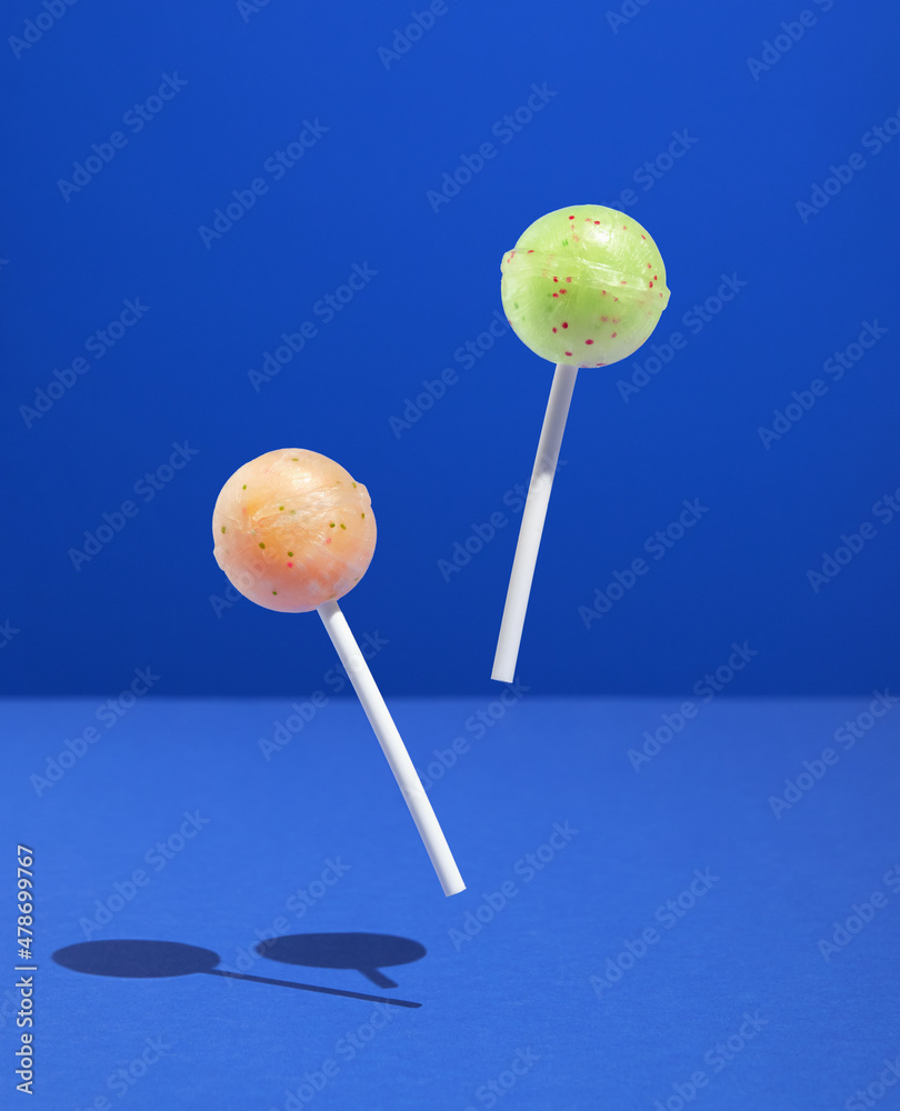Two bright lollipops on sticks hover over blue surface. Sweet inspiration and happy mood. Two bright lollipops on sticks hover over blue surface. Sweet inspiration and happy mood.