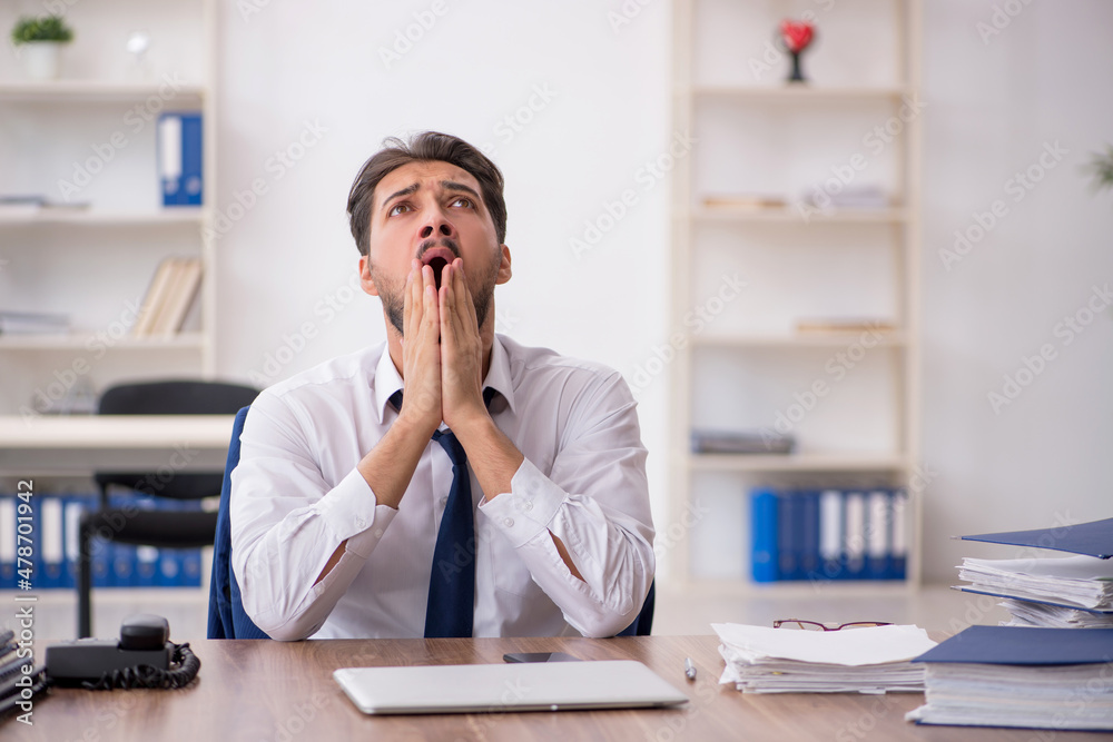 Young male employee unhappy with excessive work in the office Young male employee unhappy with excessive work in the office