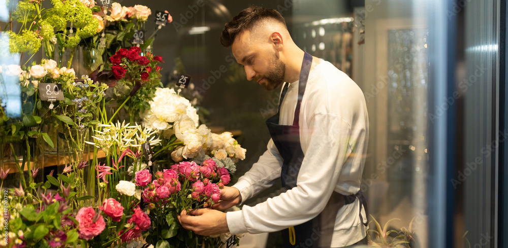 an experienced male florist in a bouquet shop examines the flowers in the fridge
