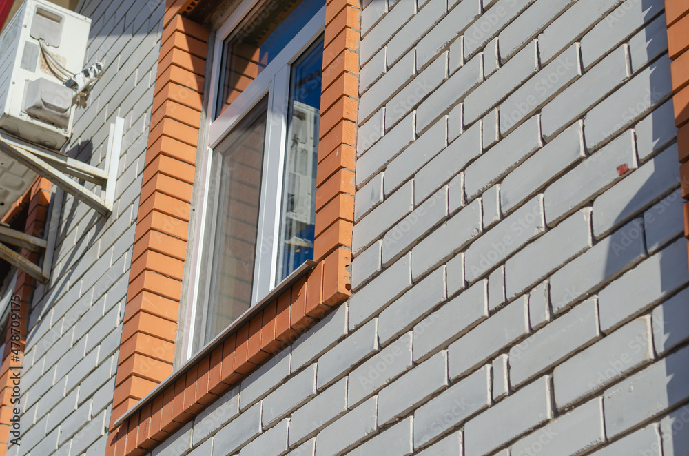 Outdoor air conditioner unit against a white brick wall. A windo