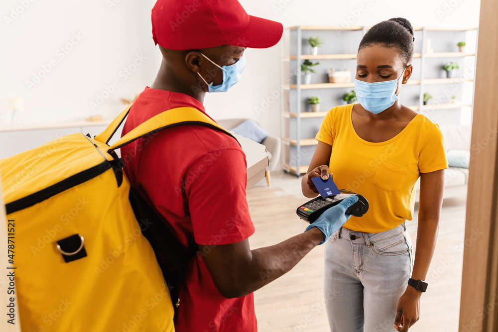 Courier Holding Terminal While Female Paying With Credit Card Indoors