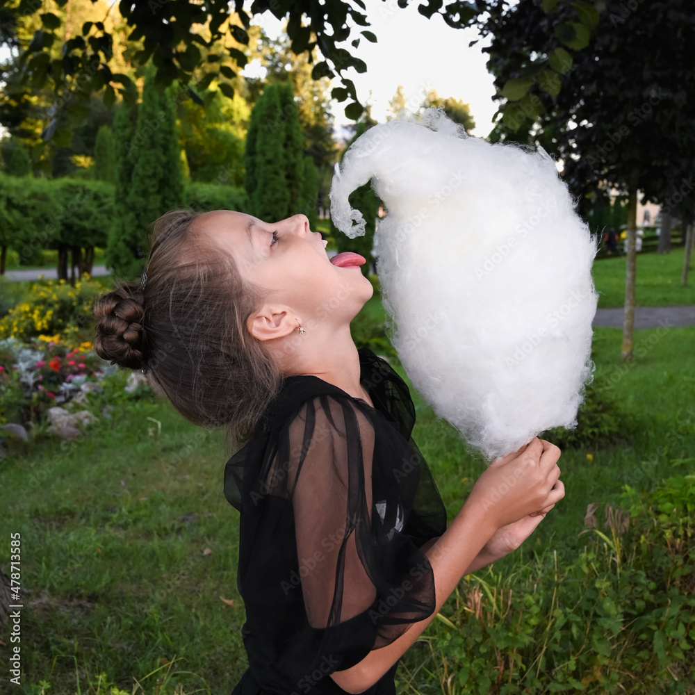 cute girl eats delicious cotton candy and has fun in the park. A happy teenage girl holds a sweet treat, dessert in her hands cute girl eats delicious cotton candy and has fun in the park. A happy teenage girl holds a sweet treat, dessert in her hands