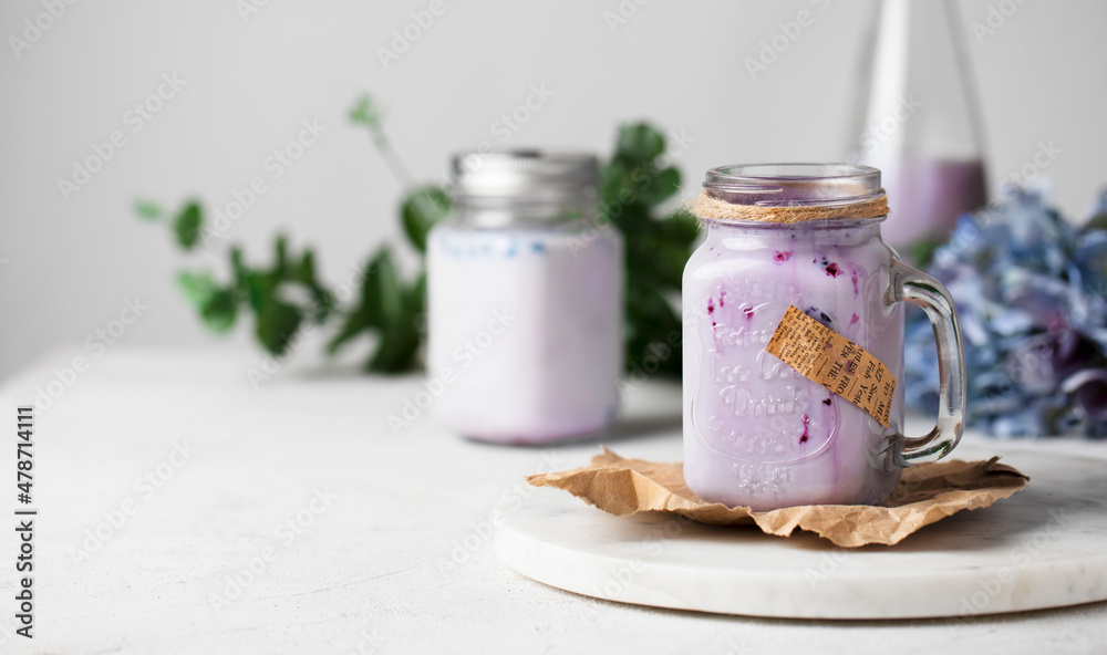 Milk black currant smoothie in a glass jar decorated with flowers on a table. Healthy milkshake beverage. Milk black currant smoothie in a glass jar decorated with flowers on a table. Healthy milkshake beverage.