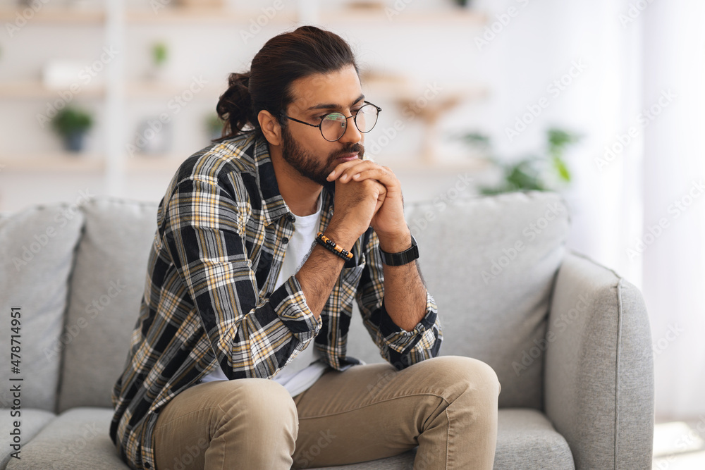 Fototapeta premium Pensive arab guy sitting on couch at home