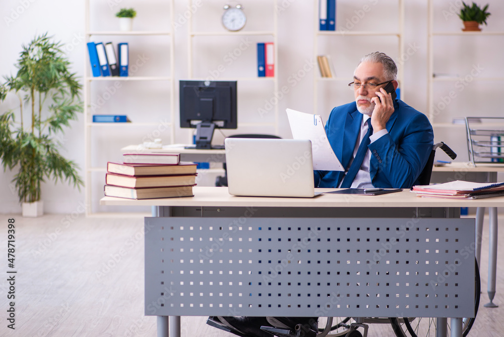 Old male employee in wheel-chair sitting in the office Old male employee in wheel-chair sitting in the office