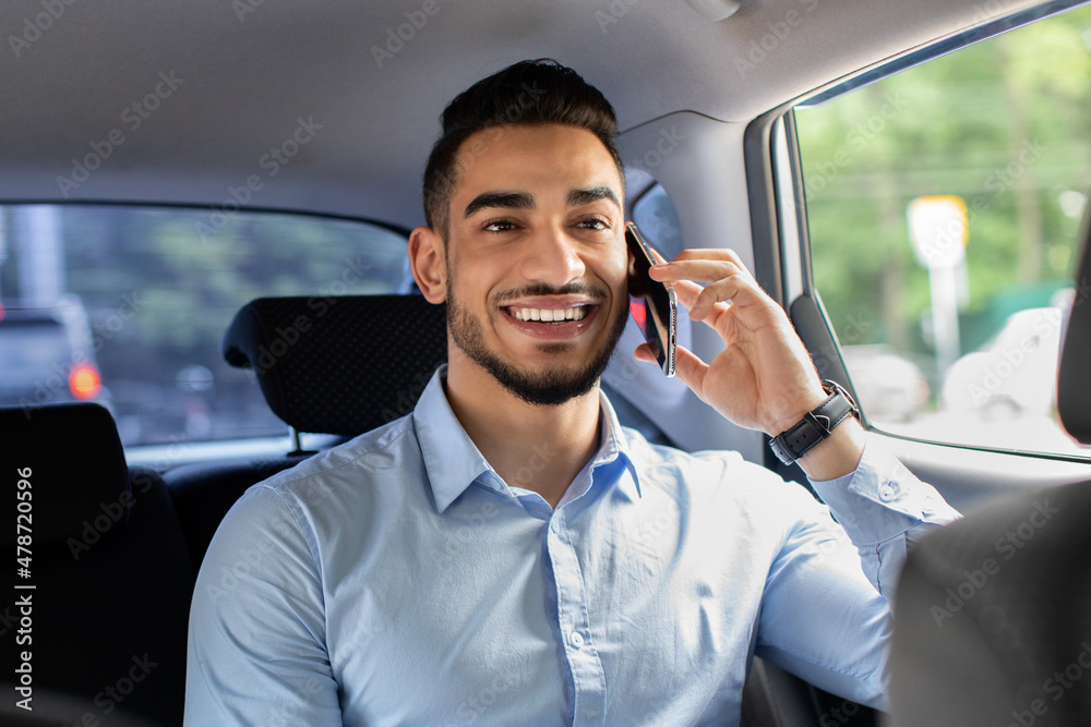 Cheerful middle-eastern manager talking to business partner on cellphone Cheerful middle-eastern manager talking to business partner on cellphone