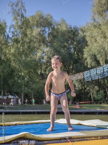 boy jumping from a trampoline into the pool. Children jump on inflatable water slide. Aqua amusement park in exotic island resort.