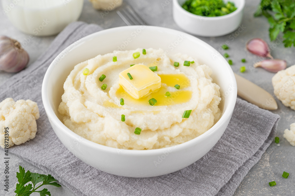 Cauliflower puree with butter and green onions in a white bowl on a gray concrete background. Healthy food. Copy space. Cauliflower puree with butter and green onions in a white bowl on a gray concrete background. Healthy food. Copy space.