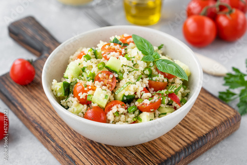 Tabbouleh salad. Couscous salad with fresh vegetables and herbs in a bowl on a gray concrete background. Copy space.