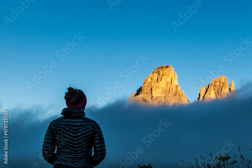 Young woman in black down jacket watching sunrise on mountain rock towers of Langkofel Group, Grohmannspitze mountain, Fuenffingerspitze mountain and Langkofel Mountain, Sella Pass, Dolomites, Italy