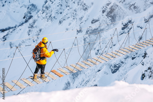 Hiker walking on rope bridge over snow mountains
