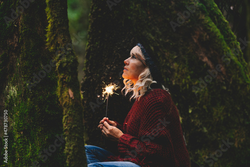 Thoughtful woman holding sparkler in woodland photo