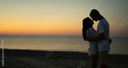 Two young lovers stand on the beach and look at each other against the backdrop of the sunset. Summer vacation concept while vacationing on a tropical beach. Baner.