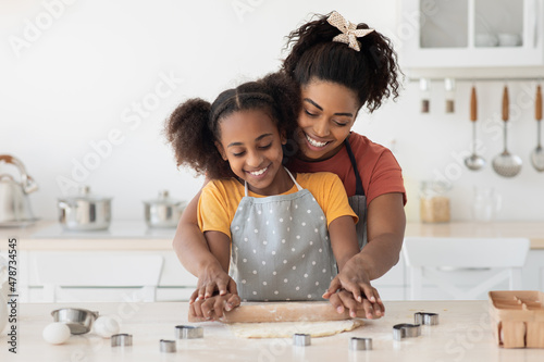 Black mom showing her teen kid hot to bake cookies