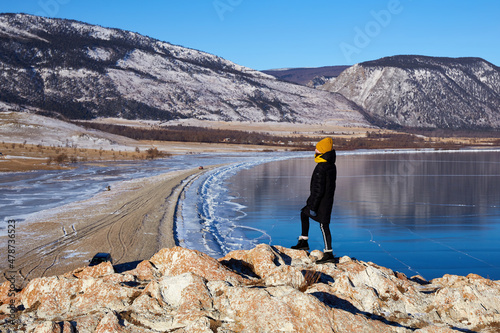 A young girl travels on Lake Baikal in winter. Beautiful winter mountain landscape  transparent ice on a sunny January day. 