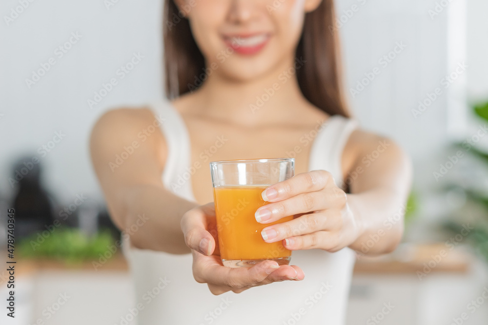 Happy housewife, smile asian young woman, girl drinking fresh orange juice in a glass drink in the kitchen, holding transparent glass in her hand, thirsty at home. Health care, healthy diet concept. Happy housewife, smile asian young woman, girl drinking fresh orange juice in a glass drink in the kitchen, holding transparent glass in her hand, thirsty at home. Health care, healthy diet concept.