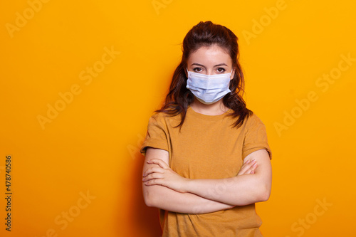 Portrait of casual woman wearing face mask against virus, looking at camera in studio. Young person having protection and safety, standing with crossed arms during coronavirus pandemic.