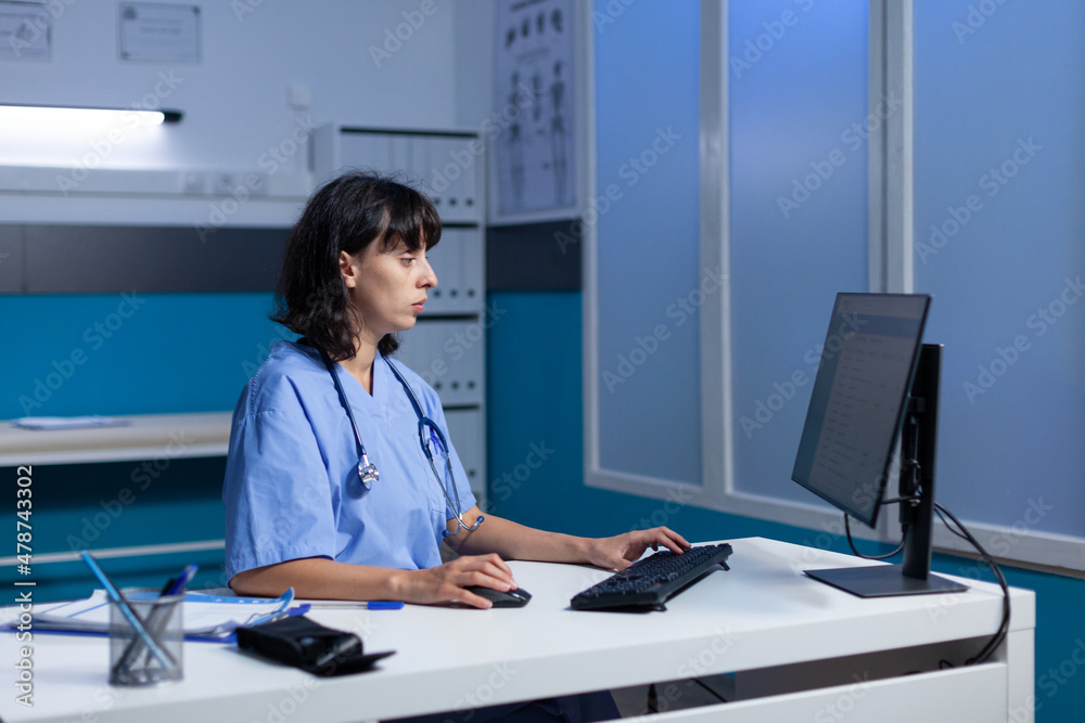 Healthcare nurse working with monitor and keyboard in doctors office. Medical assistant using computer with technology for professional support and assistance, working late at night.