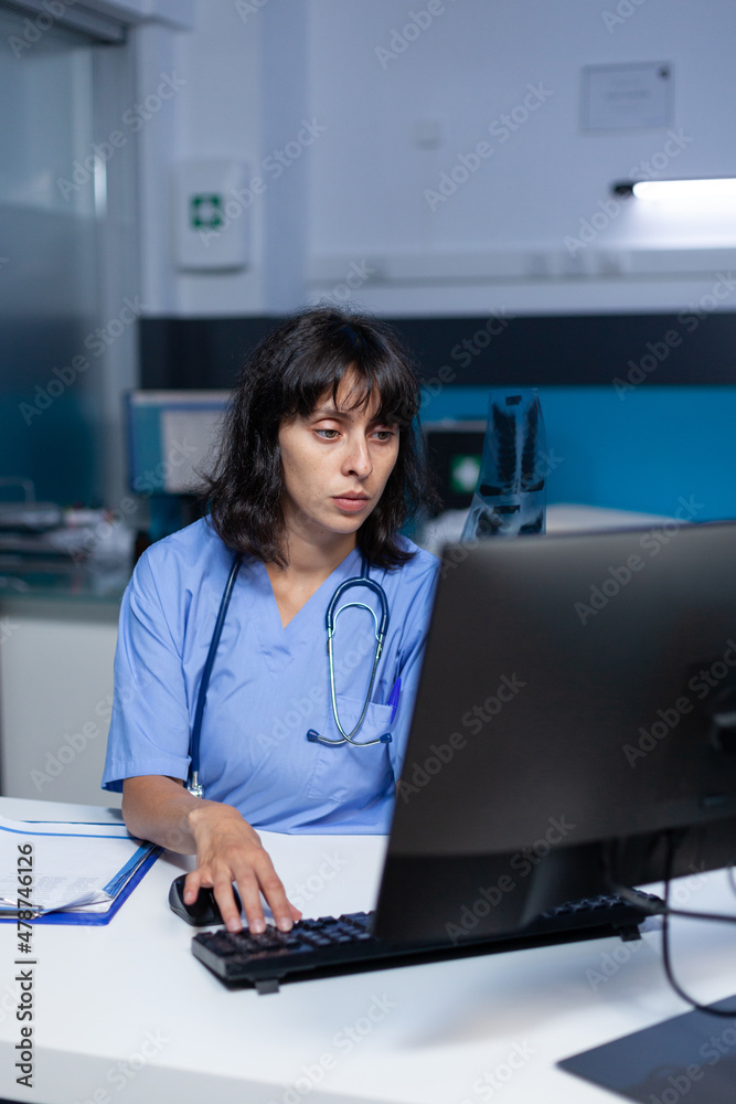 Medical assistant holding x ray scan for examination and diagnosis after hours. Nurse looking at radiography results for healthcare and medical advice, working late at night in cabinet.