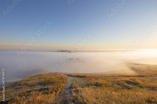 Autumn landscape in the early morning. Fog-covered expanses through which the first rays of the rising sun pass. Trees and hills in the fog. Dawn on a cold autumn morning. © Sergei