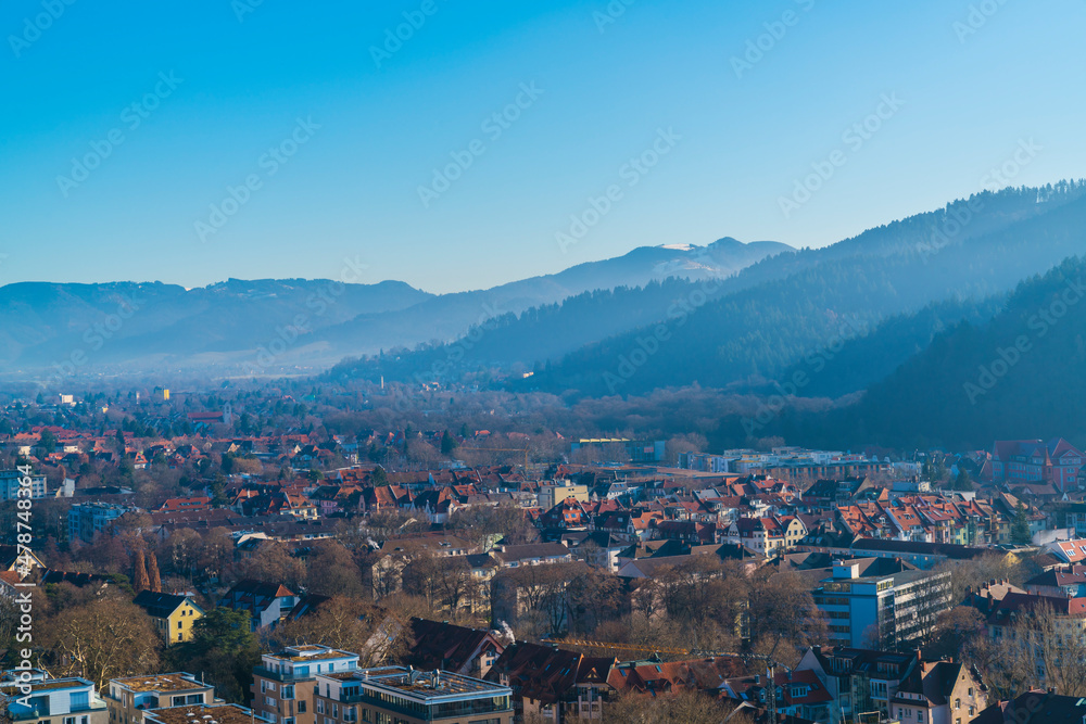 Germany, Freiburg im Breisgau cityscape houses in valley between black forest mountains schauinsland covered by snow on cold winter day