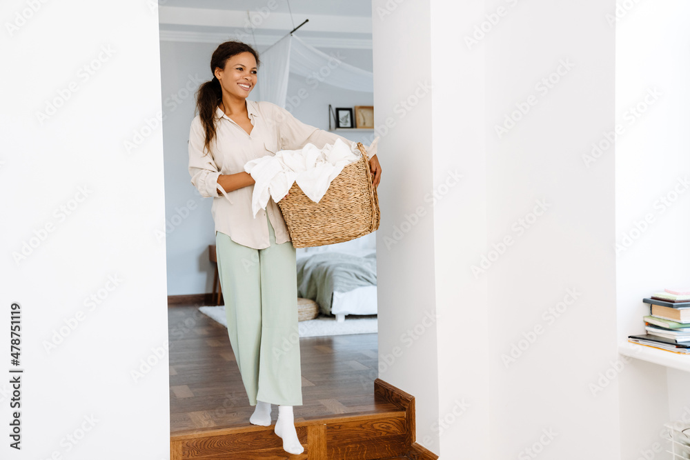 Black woman smiling while holding basket with clothes Black woman smiling while holding basket with clothes