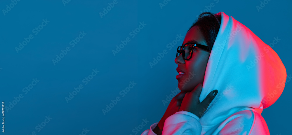 Profile view of young beautiful girl in hoodie posing isolated on gradient blue-pink background in neon. - obrazy, fototapety, plakaty 