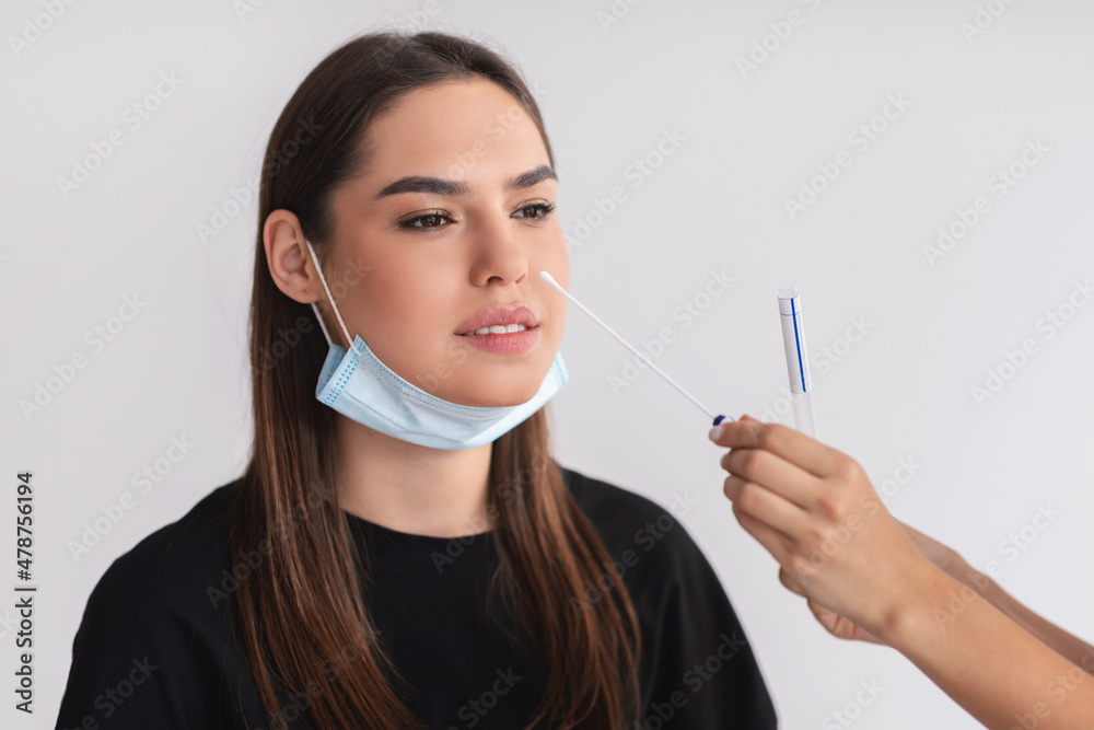 Doctor making covid-19 nasal PCR test for young female patient over light studio background Doctor making covid-19 nasal PCR test for young female patient over light studio background