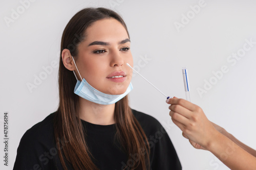 Doctor making covid-19 nasal PCR test for young female patient over light studio background