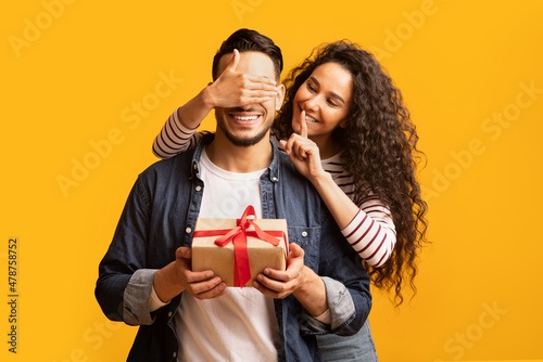Surprise Present. Romantic young arab woman covering boyfriend's eyes and giving gift