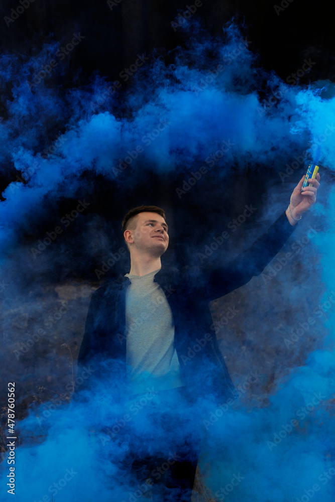 The guy holds in his hands colored smoke of blue on a black background.