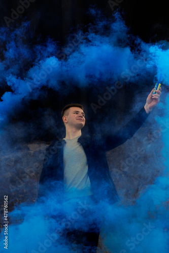 The guy holds in his hands colored smoke of blue on a black background.