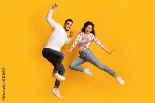 Crazy Fun. Joyful Excited Middle-Eastern Couple Jumping In Air Over Yellow Background