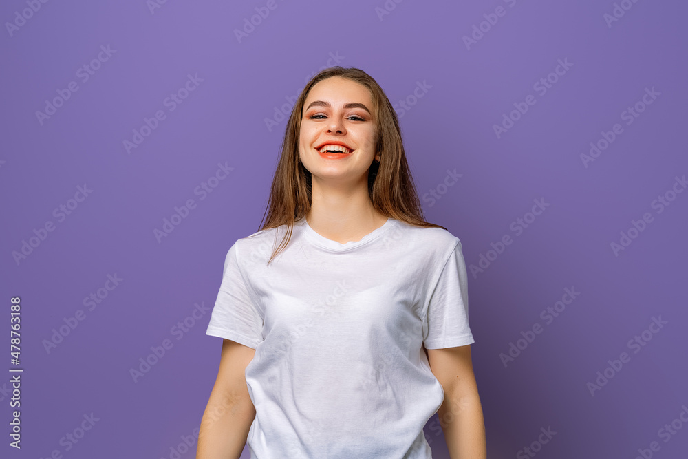 Obraz premium portrait of beautiful brunette young woman with clean skin, natural makeup looking at camera with big grin, standing over purple background