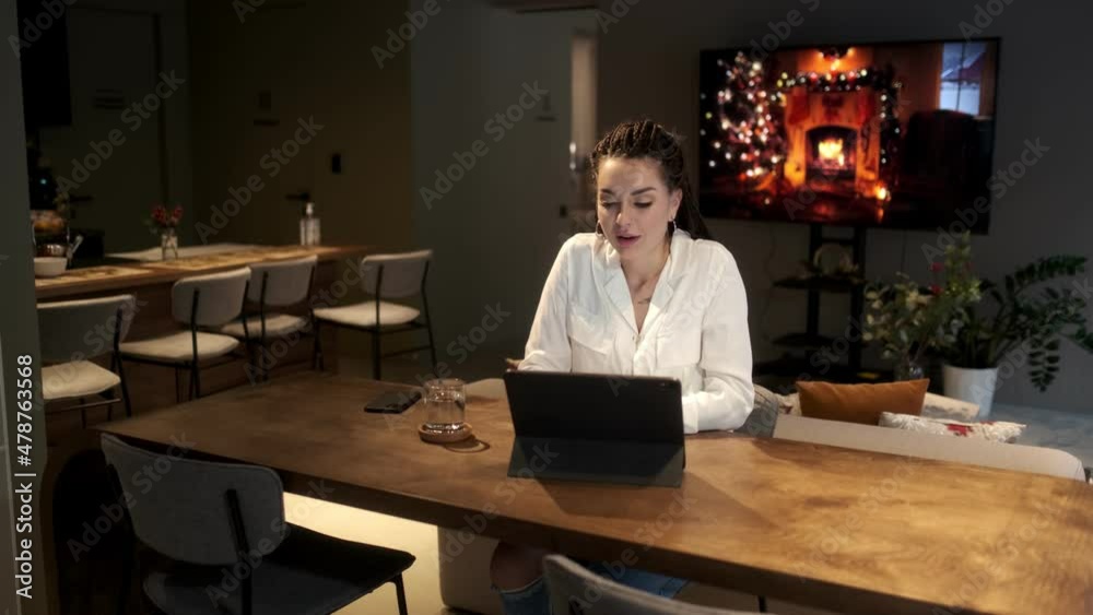 A beautiful young girl with dreadlocks sits at a table with a tablet and communicates via video link with her family. Communication concept. A beautiful young girl with dreadlocks sits at a table with a tablet and communicates via video link with her family. Communication concept.