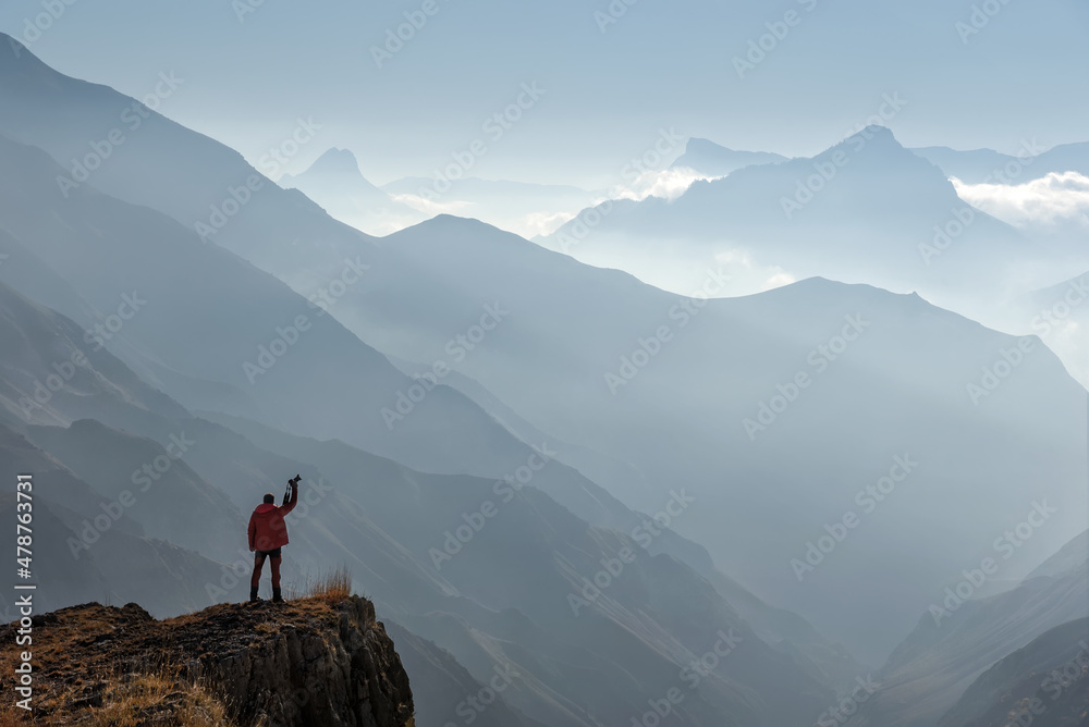 Light blue color background. The traveler stands at the edge of a cliff and raises his camera. Caucasus. Dagestan