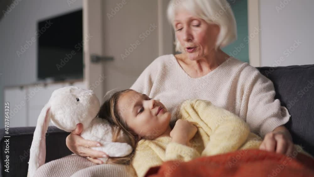 Smiling grandmother stroking her granddaughter on the head while lying on the couch Smiling grandmother stroking her granddaughter on the head while lying on the couch