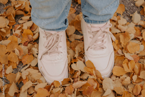 female legs in sneakers on colorful leaves in autumn Conceptual image of legs in shoes on the autumn leaves. Feet shoes walking in nature