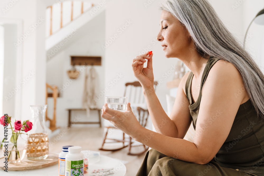 Mature asian woman taking her medication while sitting on couch Mature asian woman taking her medication while sitting on couch