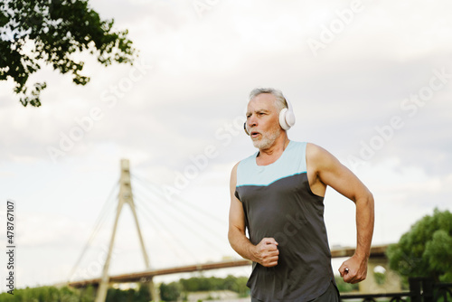 Grey senior sportsman listening music with headphones while running © Drobot Dean