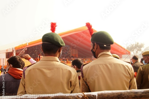 Two young security guards on duty wearing khaki uniforms with army caps, shot taken from behind. © Vibha