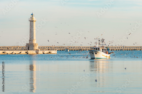Obraz na płótnie Old fishing boat returning from fishing enters the port at sunset accompanied by a flock of seagulls
