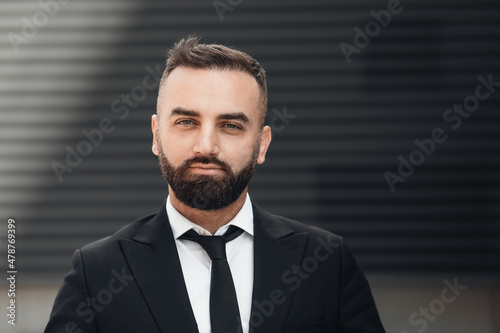 Serious middle-aged entrepreneur in suit standing in city center, looking and posing to camera. Headshot